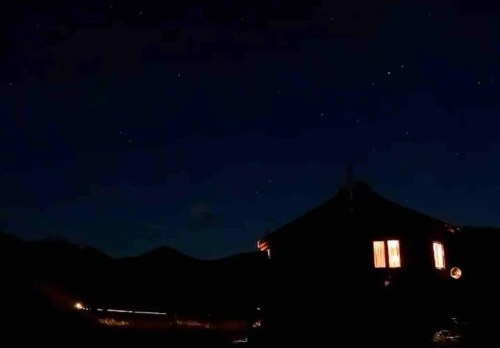 A cozy cabin illuminated at night, surrounded by mountains and a starry sky.