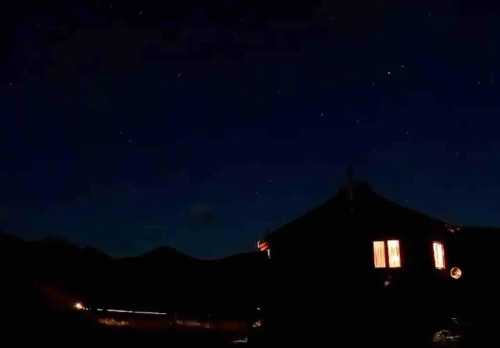 A cozy cabin illuminated at night, surrounded by mountains and a starry sky.