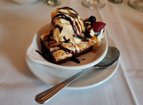 A heart-shaped dessert with ice cream, chocolate drizzle, and a strawberry on top, served on a white plate with a spoon.