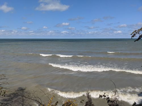 A serene view of a lake with gentle waves under a blue sky dotted with clouds.
