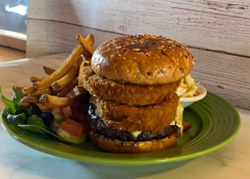 A stacked burger with onion rings, lettuce, and sauce, served with fries and a side of coleslaw on a green plate.
