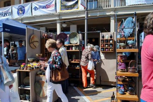 A bustling outdoor market with vendors displaying pottery and crafts, and shoppers browsing the colorful items.