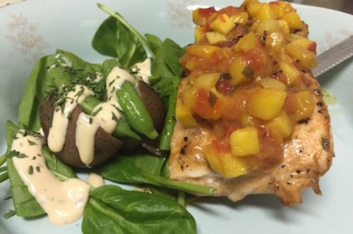 Grilled salmon topped with mango salsa, served with spinach, a baked potato, and drizzled with creamy dressing.