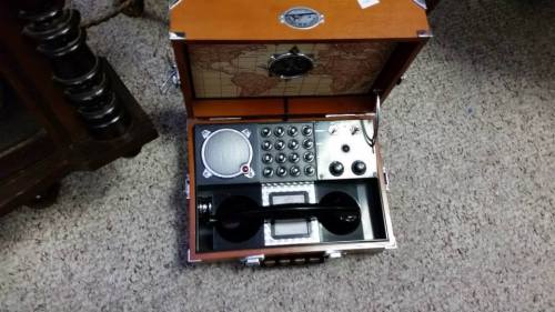 A vintage-style wooden box with a map design, containing a retro telephone and various dials and buttons.