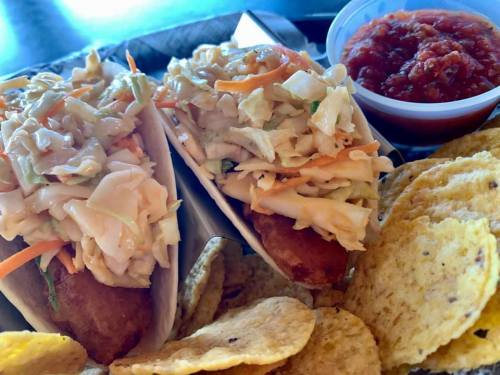 Two tacos filled with coleslaw, served with a side of salsa and a pile of tortilla chips.