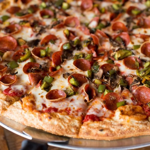 A close-up of a pepperoni pizza topped with green peppers and mushrooms, served on a metal tray.