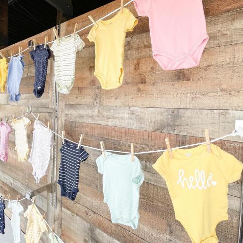 A line of colorful baby onesies hanging against a wooden backdrop.