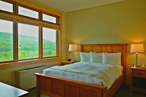 Cozy hotel room with a wooden bed, white linens, and large windows showcasing a green mountain view.