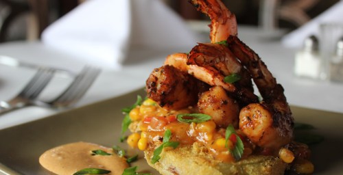 A plate of shrimp atop a corn and tomato mixture, garnished with green onions, served on a crispy base.