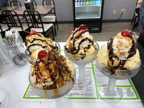 Four ice cream sundaes in glass bowls, topped with whipped cream, cherries, nuts, and chocolate sauce.