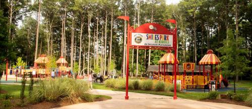 Colorful playground with various play structures, surrounded by trees and greenery, under a welcoming entrance sign.