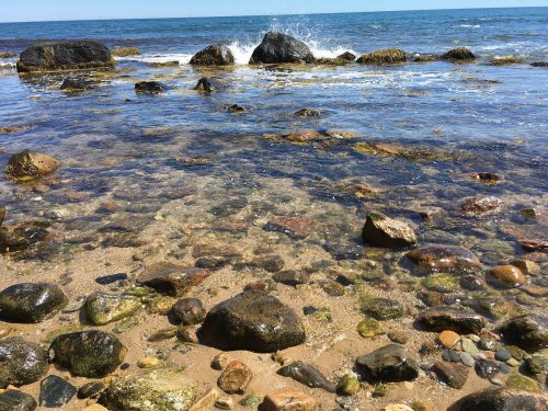 A rocky shoreline with clear water revealing pebbles and stones, waves gently crashing against the rocks.