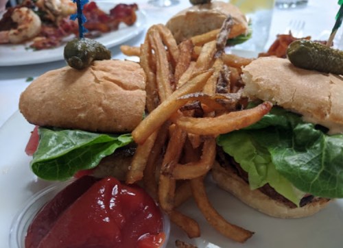 Two burgers with lettuce and pickles, served with a side of crispy fries and ketchup on a white plate.