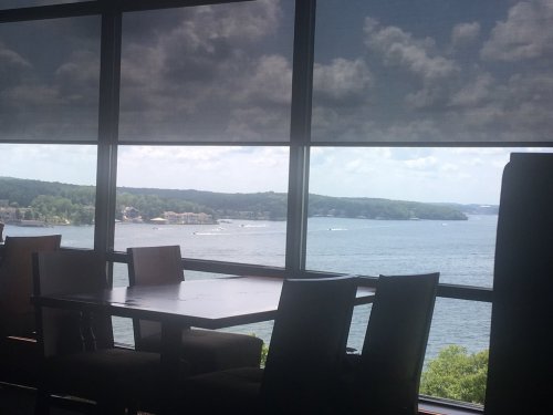 A view of a lake and hills through large windows, with a table and chairs in the foreground.