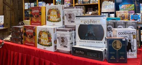 A display of various board games, including Harry Potter-themed games, arranged on a red tablecloth in a store.