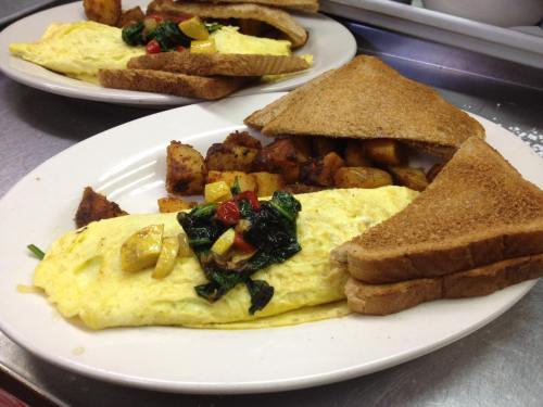 A plate with a fluffy omelette topped with vegetables, golden potatoes, and two slices of toasted bread.