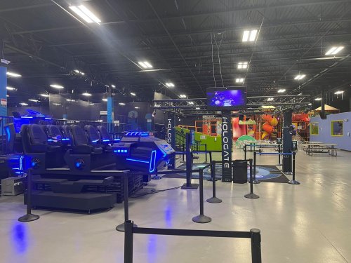 A futuristic ride with blue lighting in an entertainment center, featuring play areas and seating barriers.