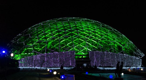 A large, illuminated dome structure at night, adorned with green and purple lights.