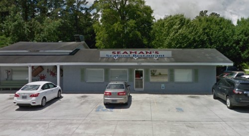 Exterior view of Seaman's Seafood Restaurant, featuring a sign, parking lot, and surrounding trees.