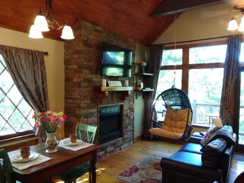 Cozy living space with a stone fireplace, hanging chair, and large windows overlooking nature. Flowers on the table.