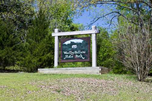 Sign for Woolly Hollow State Park, surrounded by greenery and trees under a clear blue sky.