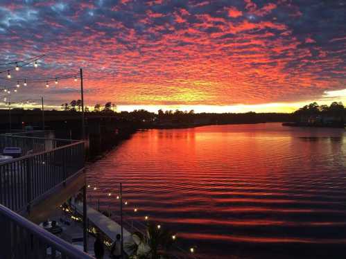 A vibrant sunset over a calm lake, with colorful clouds reflecting on the water and string lights in the foreground.