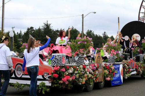 A colorful parade float adorned with flowers, featuring people waving and dressed in festive attire.