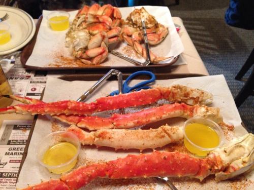 A table with two plates of crab legs, one with whole crabs, and small cups of melted butter for dipping.