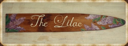 A wooden sign with the text "The Lilac" and painted lilac flowers on a rustic background.