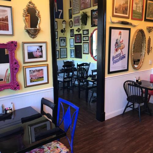 A cozy restaurant interior with colorful walls, framed art, and black wooden chairs. A vibrant blue chair stands out.