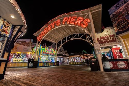 Brightly lit entrance to Morey's Piers at night, featuring colorful attractions and games along a wooden boardwalk.