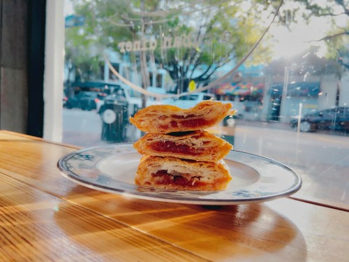 A stack of flaky pastries on a plate, illuminated by sunlight, with a city street visible through the window.