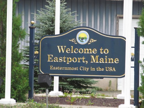 Sign welcoming visitors to Eastport, Maine, noting it as the easternmost city in the USA. Greenery in the background.