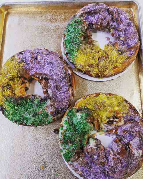 Three colorful King Cakes with purple, green, and yellow sugar sprinkles on a silver tray.