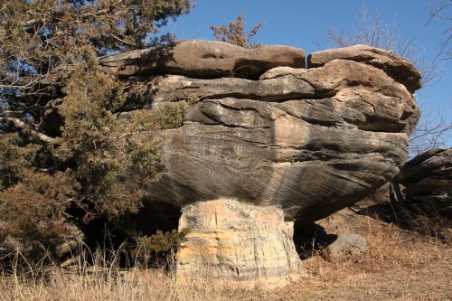 A large, mushroom-shaped rock formation stands amidst sparse vegetation under a clear blue sky.