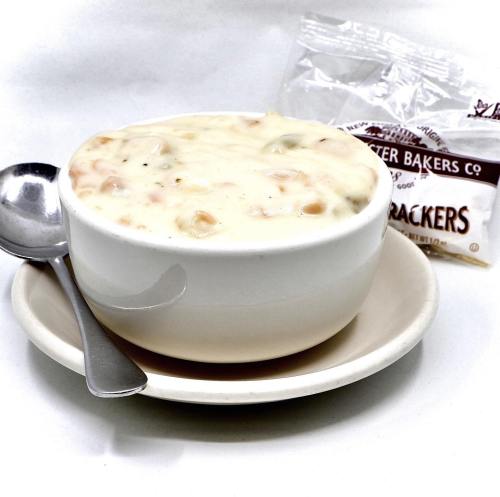 A bowl of creamy soup with a spoon, served on a plate, alongside a packet of crackers.