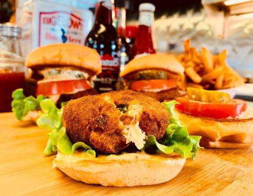 A close-up of a burger with lettuce and tomato, surrounded by other burgers and fries on a wooden surface.