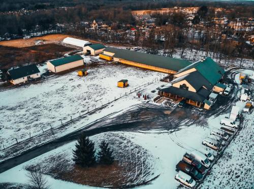 Aerial view of a snowy farm with several buildings, vehicles, and a surrounding landscape of trees and fields.