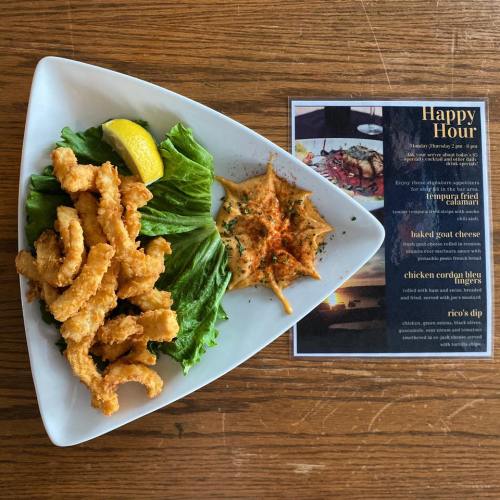 A plate of fried calamari with lemon and lettuce, alongside a menu for happy hour appetizers.