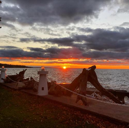 Sunset over a lake, with clouds and silhouettes of driftwood along the shore, creating a serene atmosphere.