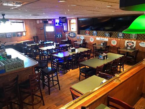 A spacious restaurant interior with wooden floors, tables, and chairs, featuring bar signs and a large TV.