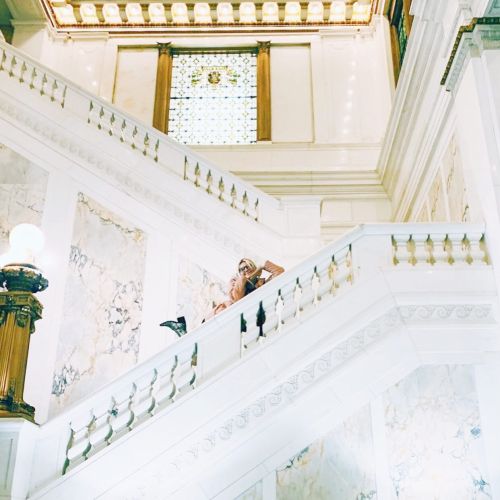 A grand staircase with marble walls and ornate details, featuring a person in elegant attire ascending the steps.