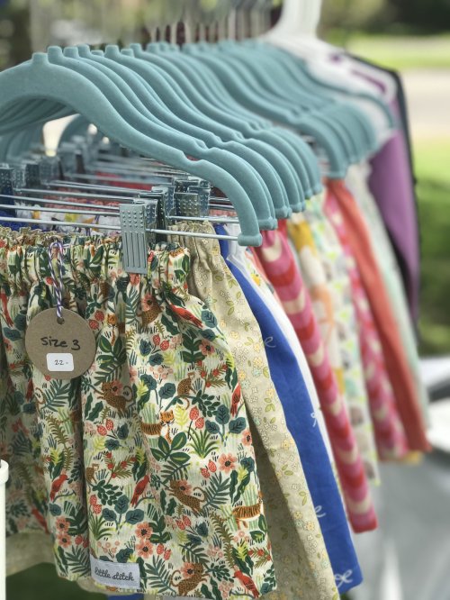 Colorful children's skirts hanging on blue hangers, labeled with sizes and patterns, displayed outdoors.