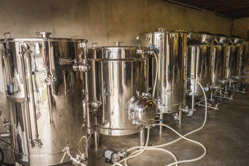 A row of shiny stainless steel brewing tanks in a dimly lit industrial space.
