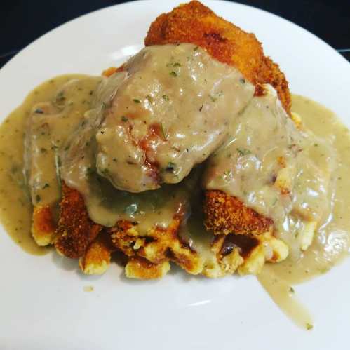 A plate of crispy fried chicken topped with creamy gravy, served over a bed of fluffy mashed potatoes.