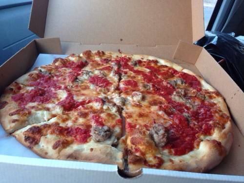 A pizza in a cardboard box, topped with tomato sauce, cheese, and sausage, partially sliced.