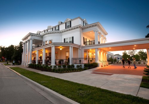 A large white building with columns, illuminated at dusk, featuring a porch and landscaped surroundings.