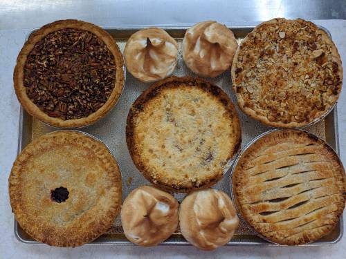 A tray of assorted pies, including pecan, apple, and meringue, arranged neatly on a countertop.