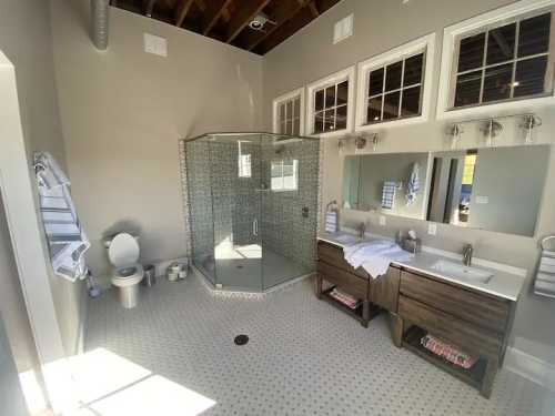 Spacious bathroom featuring a glass shower, dual sinks, modern fixtures, and large windows for natural light.