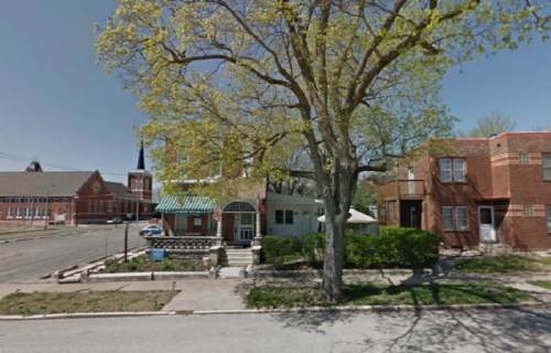 A street view featuring a tree, a small building, and brick structures in a quiet neighborhood.